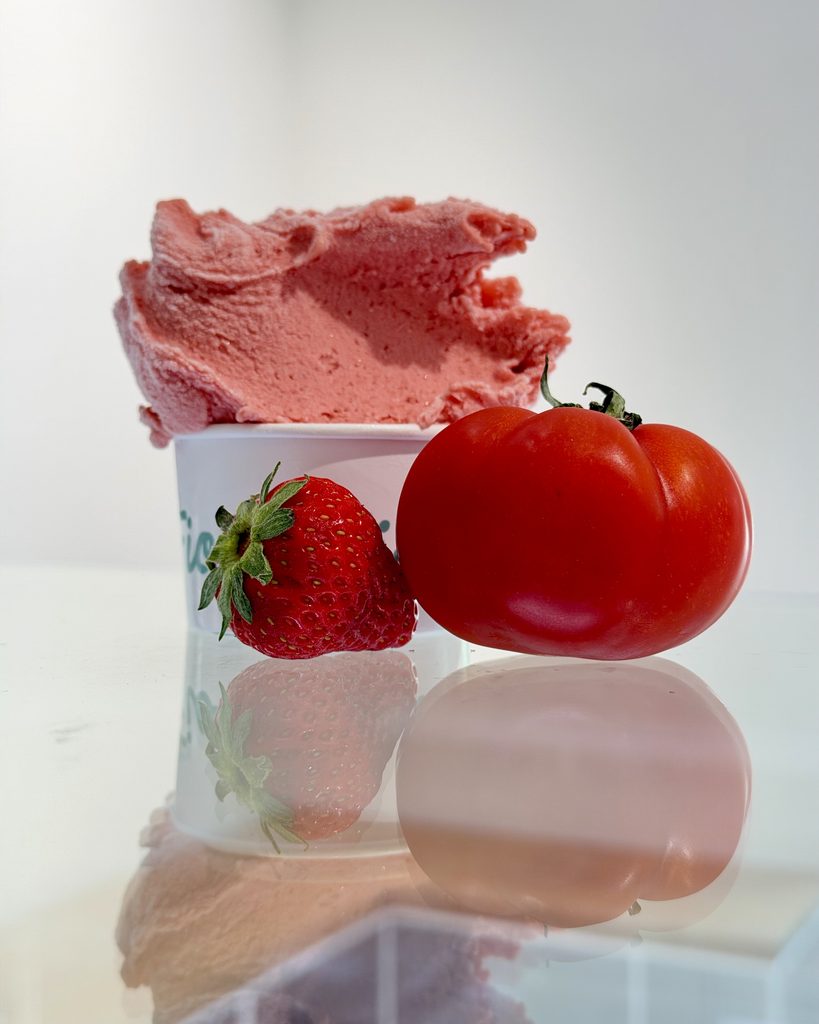 Gelato fragola e pomodoro in coppetta, accanto a una fragola e a un pomodoro