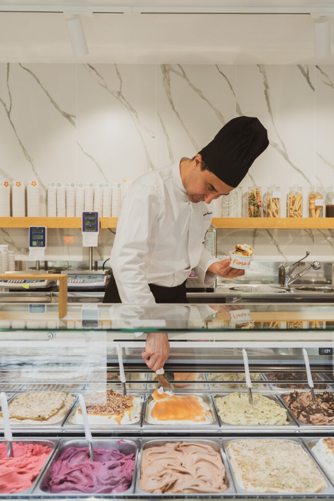 Roberto Comelli al banco della gelateria serve una coppetta di gelato davanti alla vetrina dei gusti